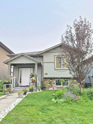 A residential house with a front porch, potted plants, and a well-maintained lawn. - Home Sweet Home Away From Home (Red Deer)