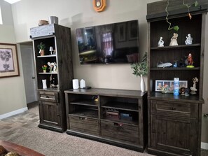 A living room with a dark wood entertainment center, a flat-screen TV, and various decorative items. - Home Sweet Home Away From Home (Red Deer)