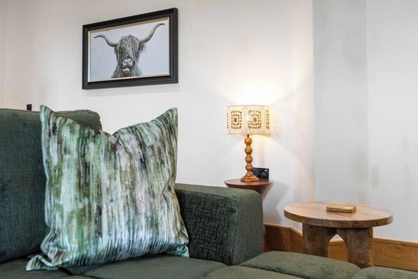 A room with a green sofa, a framed artwork on the wall, a table lamp, and a small wooden table. - Spacious Luxury Barn| Countryside Stay in Newburgh (Wigan)