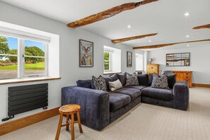 A modern living room with a sectional sofa, wooden beams, and a view of the outdoors. - Spacious Luxury Barn| Countryside Stay in Newburgh (Wigan)