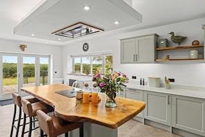 A modern kitchen with a central island, bar stools, and a view of the outdoors. - Spacious Luxury Barn| Countryside Stay in Newburgh (Wigan)