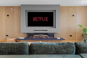 A modern living room with a large flat-screen TV mounted above a fireplace, a sofa, and a potted plant. - Spacious Luxury Barn| Countryside Stay in Newburgh (Wigan)