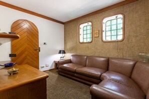 A room with a herringbone-patterned door, a brown leather sofa, and two windows with wooden frames. - 5 QTS Fut Tenis Sauna Boate 30min SP (Carapicuíba)