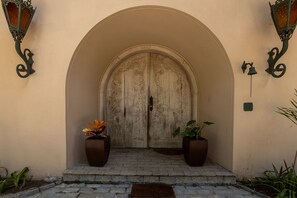 A wooden door with a decorative archway, two potted plants on either side, and a small bell on the right. - 5 QTS Fut Tenis Sauna Boate 30min SP (Carapicuíba)