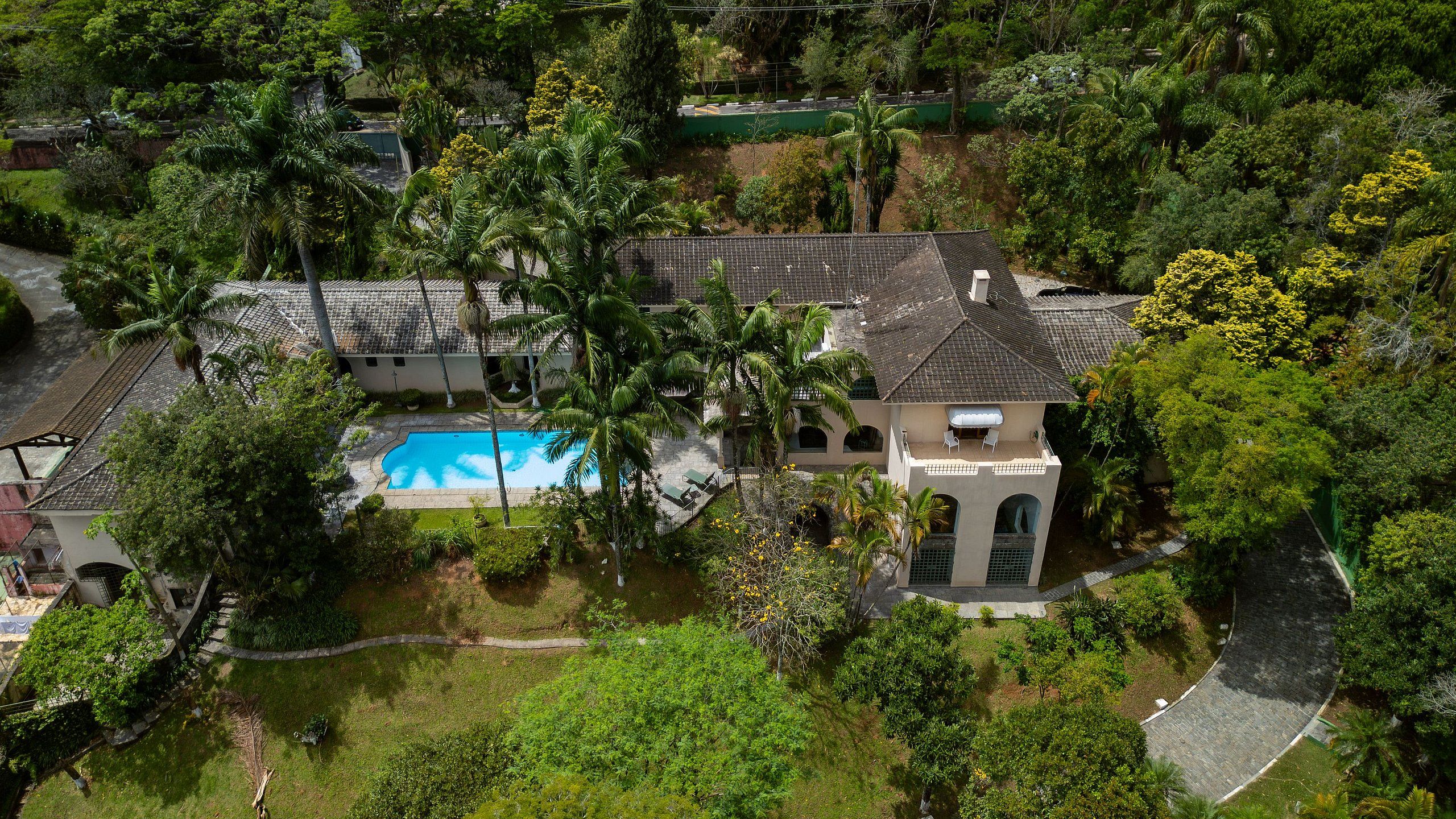 A residential property with a swimming pool, multiple buildings, and lush greenery.