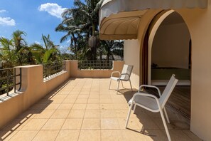 Ein Balkon mit zwei weißen Stühlen, gefliestem Boden und Blick auf Palmen.