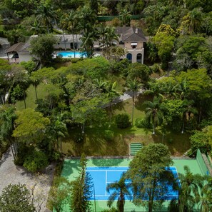 An aerial view of a residential area with a swimming pool, tennis court, and lush greenery. - 5 QTS Fut Tenis Sauna Boate 30min SP (Carapicuíba)
