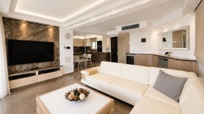 A modern living room with a flat-screen TV, a white sofa, and a coffee table with decorative items. - Trident Luxury Beach Apt by TrulyCyprus (Paralimni)