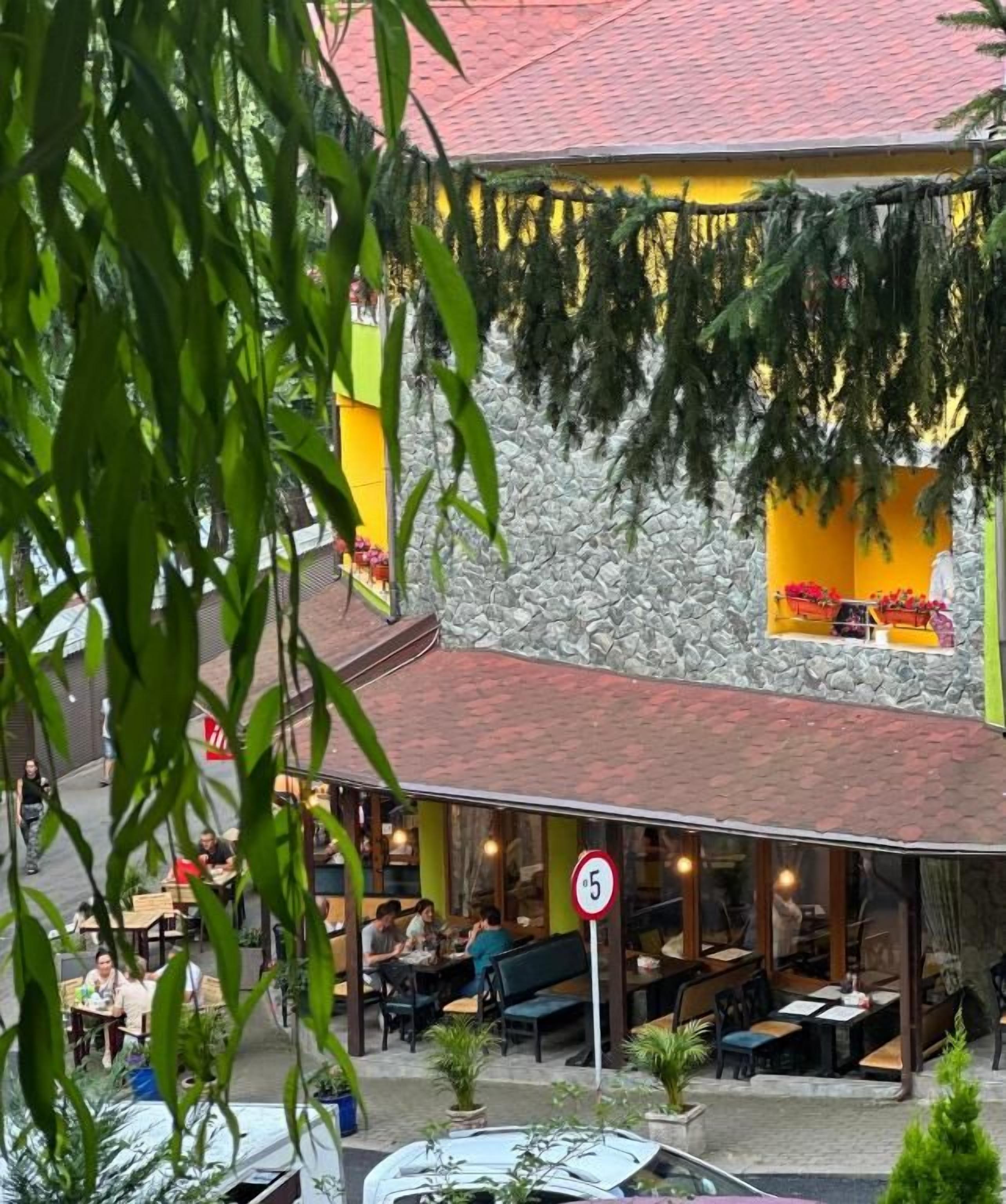 An outdoor dining area with tables and chairs, a stone wall, and a red roof.