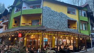 A two-story building with a restaurant on the ground floor, outdoor seating, and a stone facade.