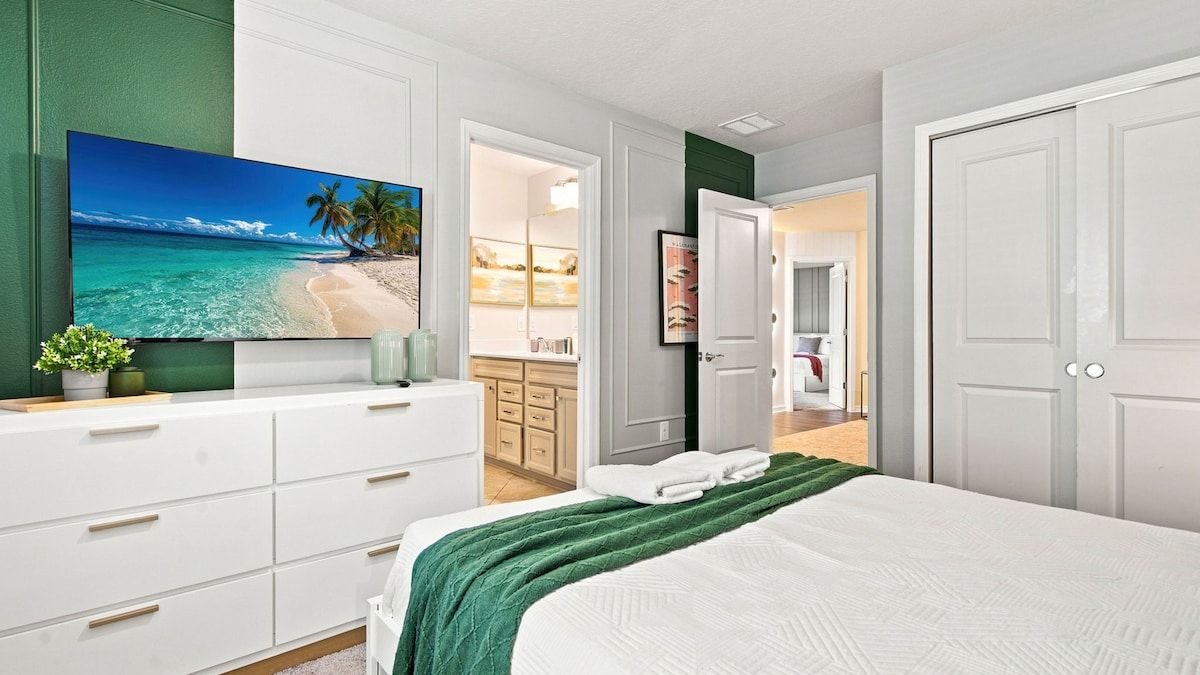 A bedroom with a bed, a TV, a dresser, and a door leading to a bathroom.