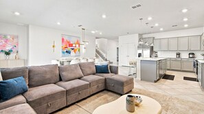 A modern living room with a sectional sofa, a dining area, and a kitchen with white cabinets. - 10BR Luxury Villa, Pool & Hot Tub, Windsor Cay (Clermont)