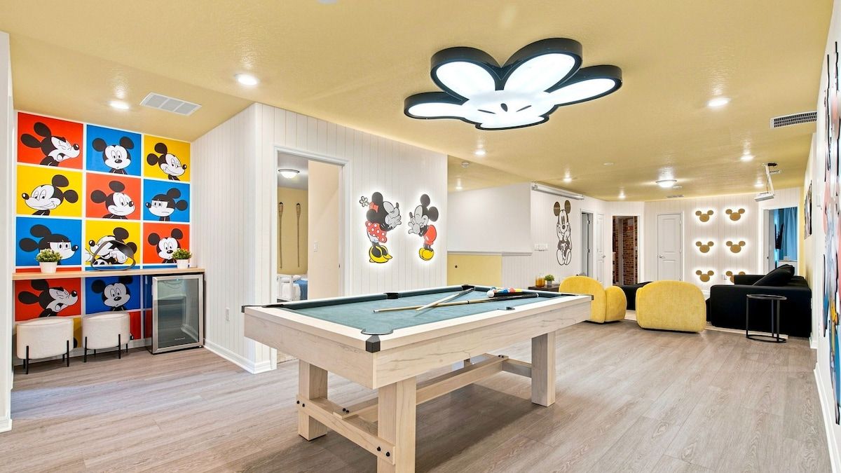 Una mesa de billar en una habitación con una lámpara en el techo y una pared decorada con diseños de Mickey Mouse.