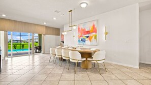 A dining area with a round table, white chairs, and a large abstract painting on the wall. - 10BR Luxury Villa, Pool & Hot Tub, Windsor Cay (Clermont)