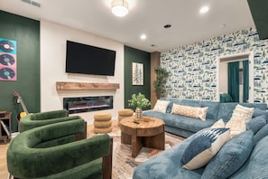Ein Wohnzimmer mit Kamin, grünen Sesseln, einem blauen Sofa und einem an der Wand befestigten Fernseher.
