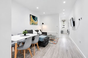 A modern living room with a dining area, a sofa, a coffee table, and a painting on the wall.