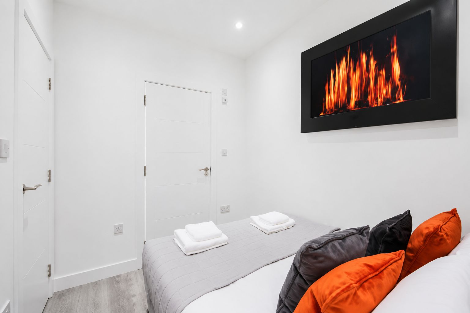 A bedroom with a bed, pillows, a wall-mounted TV, and a door.
