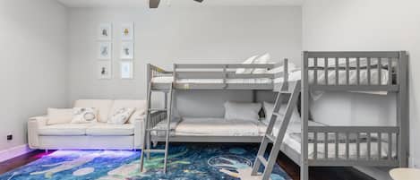 A child's bedroom with bunk beds, a ceiling fan, a white sofa, and a space-themed carpet.