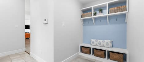 A hallway with a white wall, a blue curtain, and a white bench with baskets.