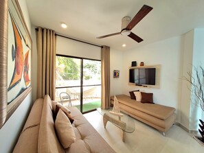 Ein modernes Wohnzimmer mit einer Couch, einem Glastisch, einem an der Wand befestigten Fernseher und einem Deckenventilator.