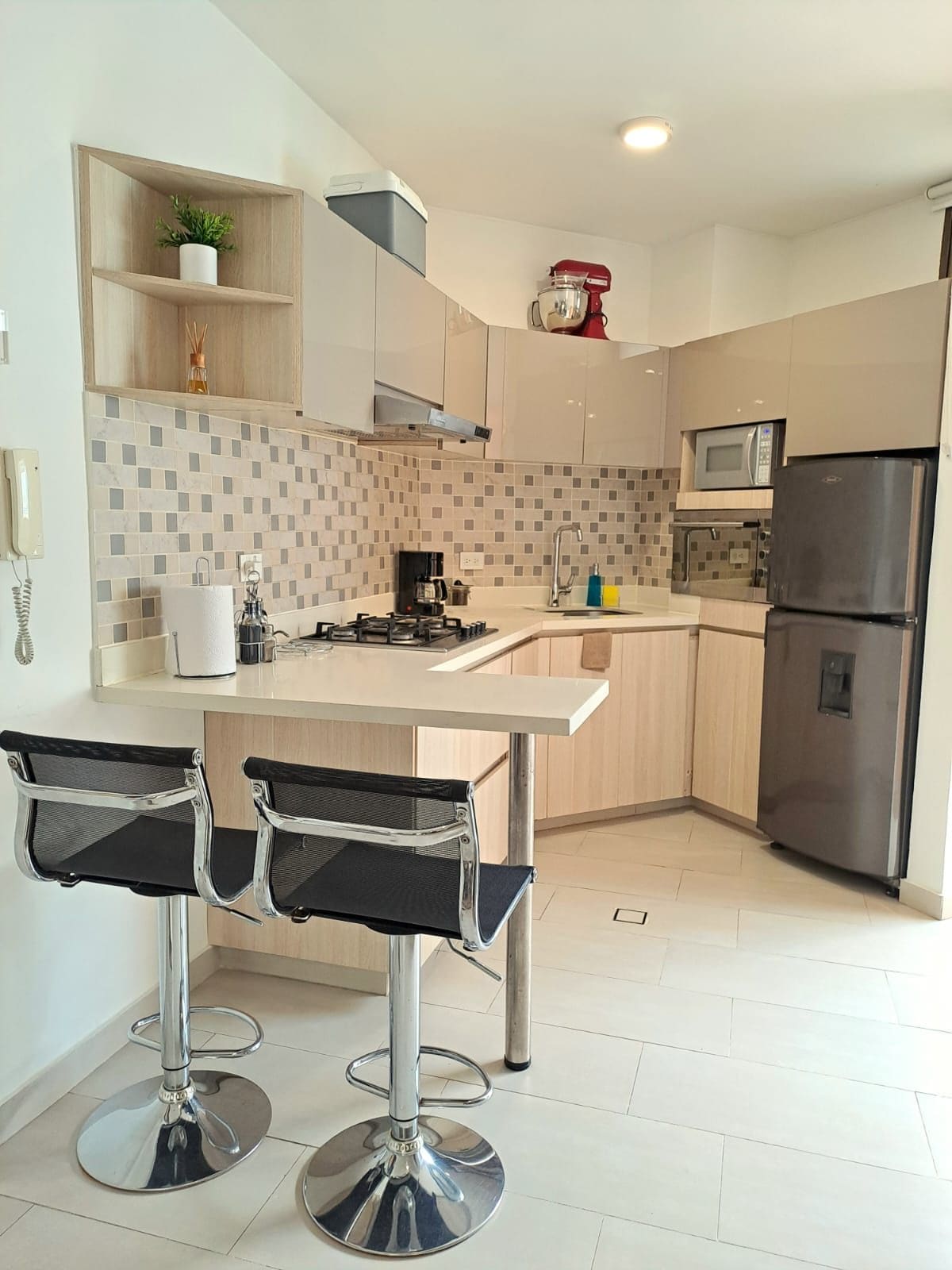 A modern kitchen with a central island, bar stools, a microwave, and a refrigerator.