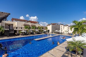 A swimming pool area with lounge chairs and umbrellas, surrounded by buildings with a tropical architectural style. - Private Pool on Luxury Penthouse (Playa del Carmen)