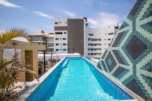A swimming pool with a view of modern buildings and a palm tree. - Steps From the Bucerias Beach With Rooftop Pool (Bucerías)