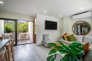 A modern living room with a sofa, a dining area with chairs, a flat-screen TV mounted on the wall, and a large mirror. - Steps From the Bucerias Beach With Rooftop Pool (Bucerías)