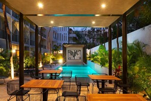 An outdoor seating area with tables and chairs, a pool, and a view of a building with balconies. - Private Pool With Great Comfort (Tulum)