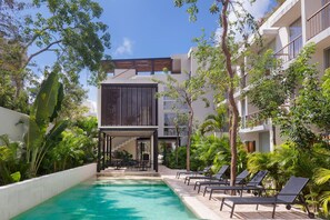 A modern building with a pool, surrounded by lush greenery and palm trees. - Private Pool With Great Comfort (Tulum)