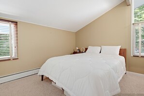 A bedroom with a large bed, two bedside tables, and a window with blinds. - The Après Chalet | Steps to Mount Snow w Fireplace (Dover)