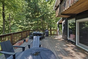 A wooden deck with outdoor furniture, surrounded by trees. - The Après Chalet | Steps to Mount Snow w Fireplace (Dover)