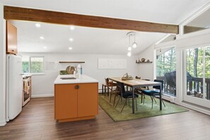 A modern kitchen with an island, wooden ceiling beams, and a dining area with chairs and a table. - The Après Chalet | Steps to Mount Snow w Fireplace (Dover)