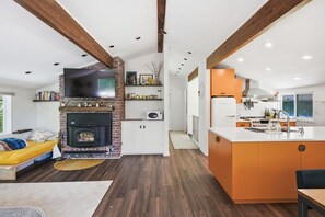 A modern kitchen with a central island, a built-in oven, and a flat-screen TV above the fireplace. - The Après Chalet | Steps to Mount Snow w Fireplace (Dover)