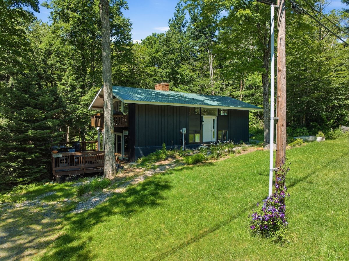 Eine Hütte mit einem grünen Dach, umgeben von Bäumen und einem grünen Rasen.