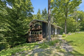Eine Holzhütte mit einer Terrasse, umgeben von Bäumen und einem Kiesweg.