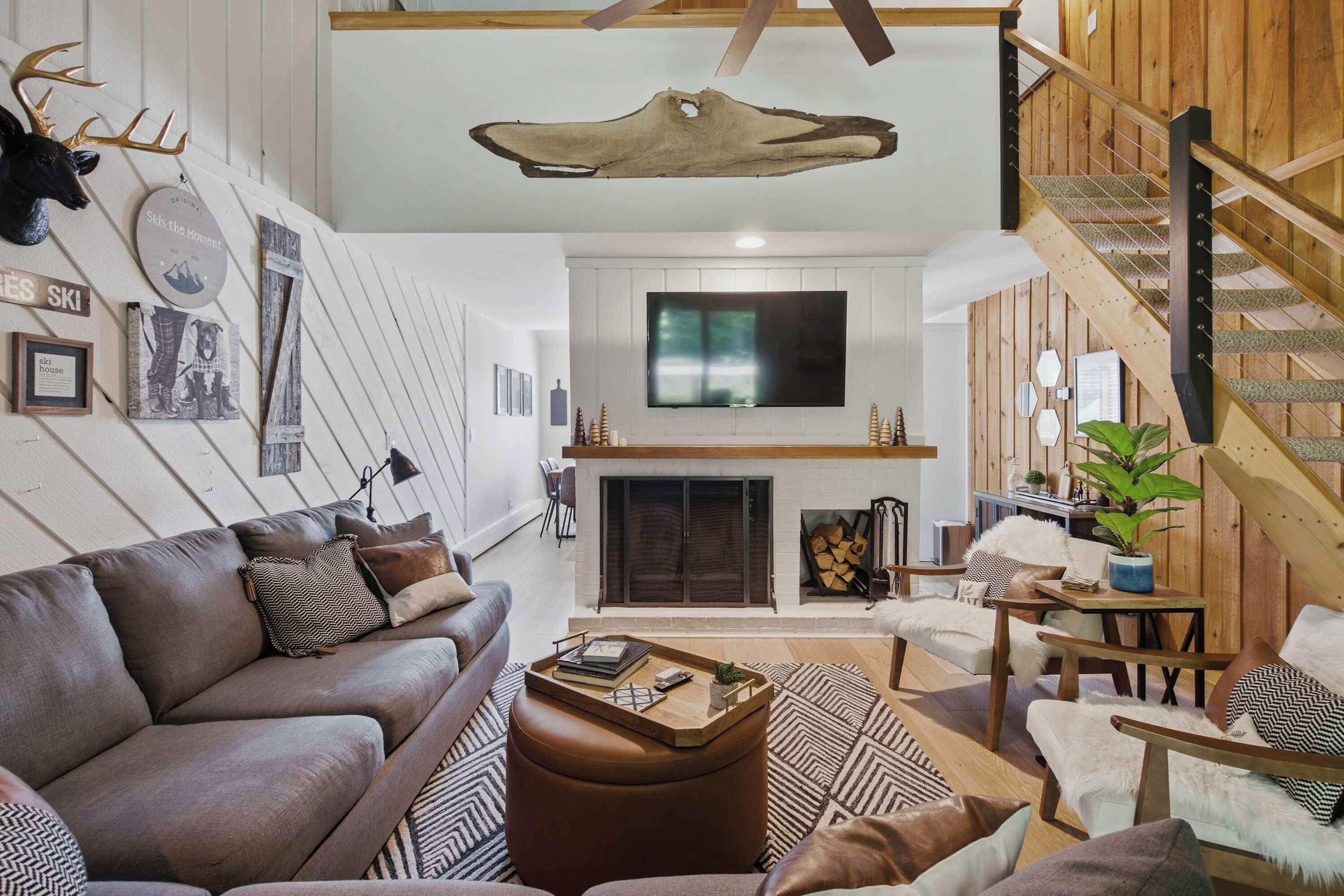 A modern living room with a fireplace, a mounted TV, and a wooden staircase.