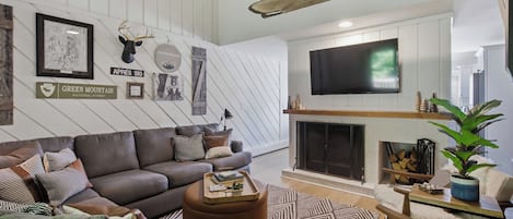 A modern living room with a fireplace, a mounted TV, and a variety of wall decorations including a deer head and a sign for Green Mountain National Forest.