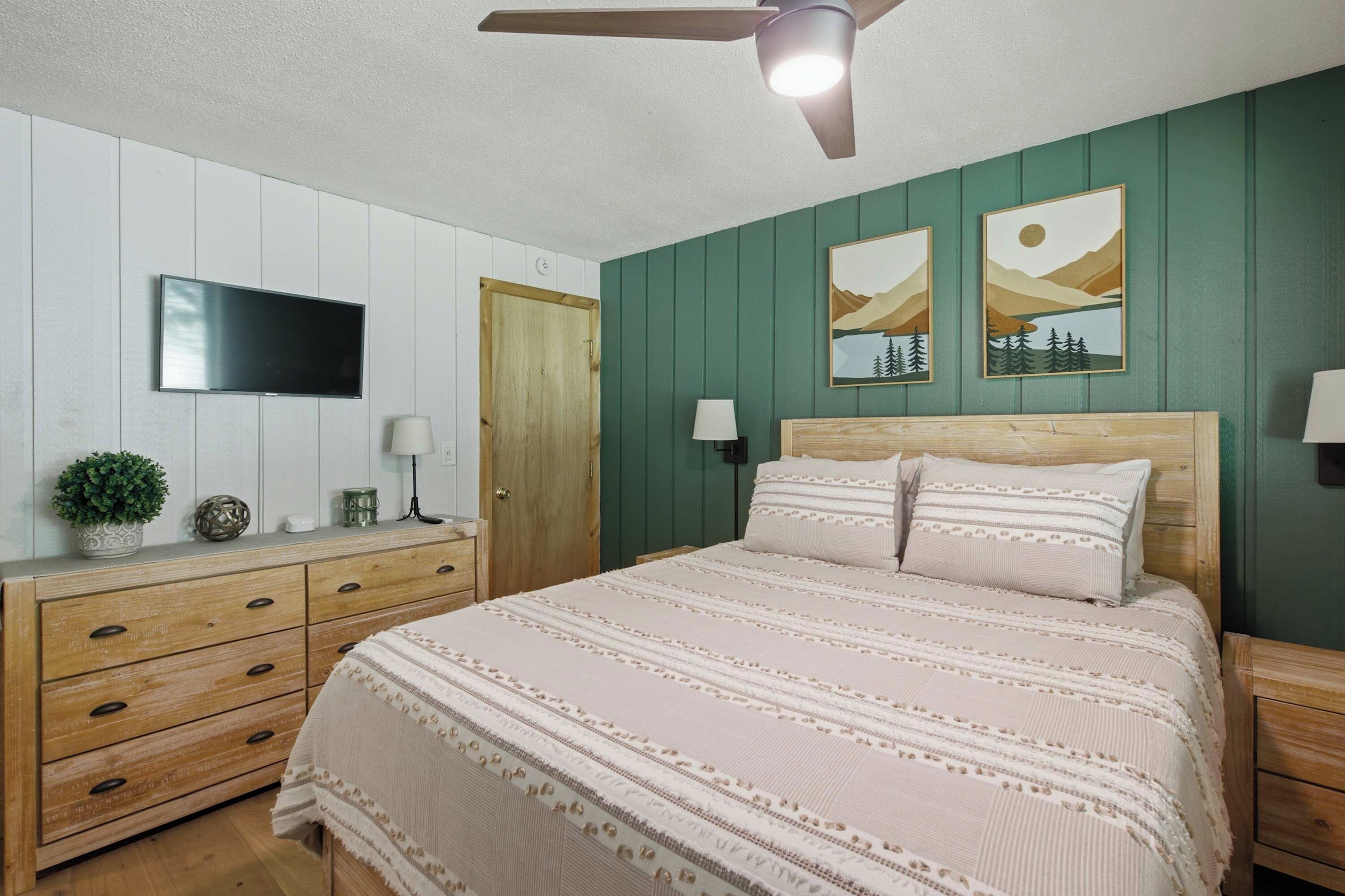 A bedroom with a bed, a dresser, a television, and two wall-mounted paintings.