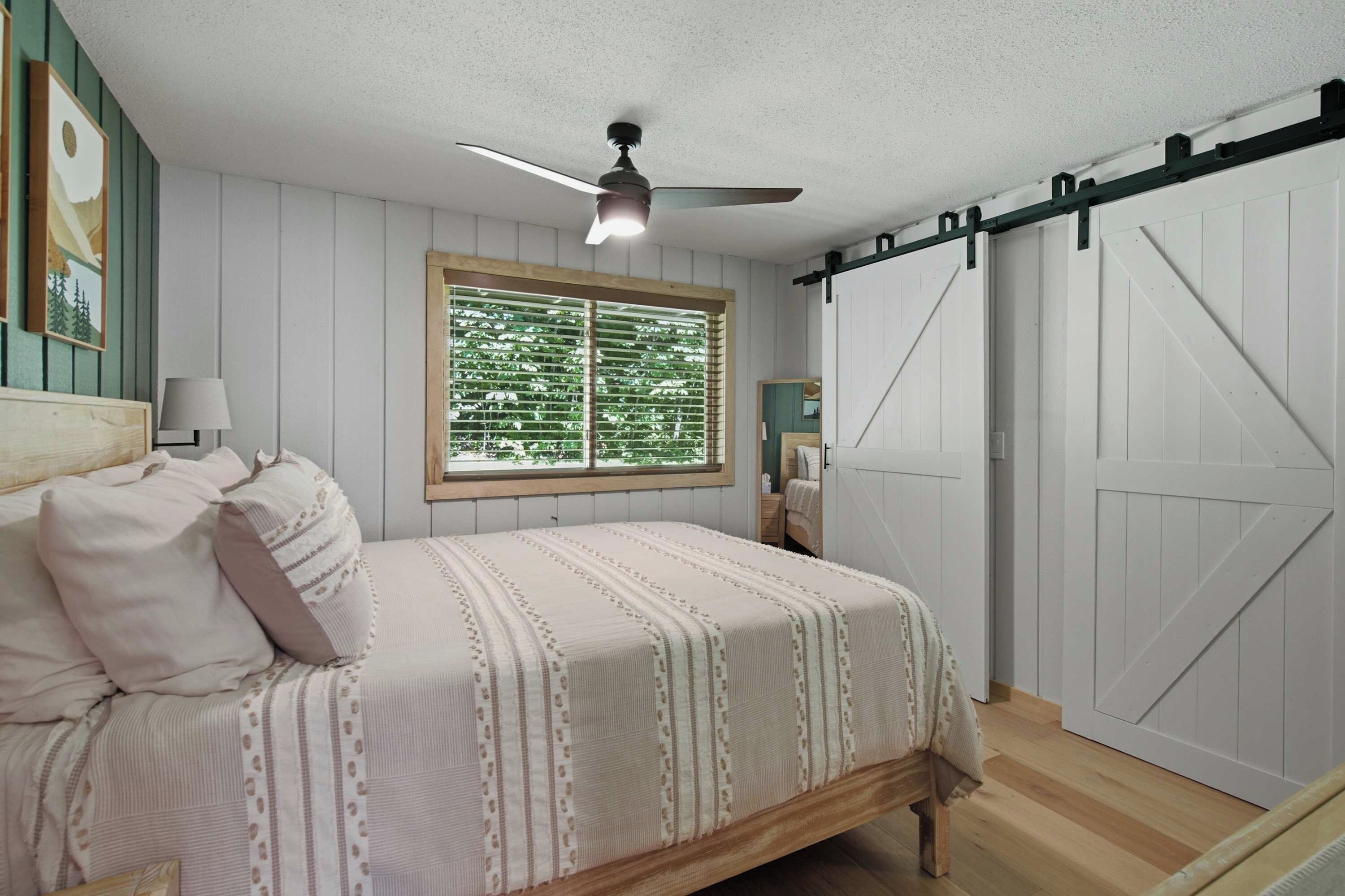 A bedroom with a bed, a window with blinds, a ceiling fan, and a sliding barn-style door.