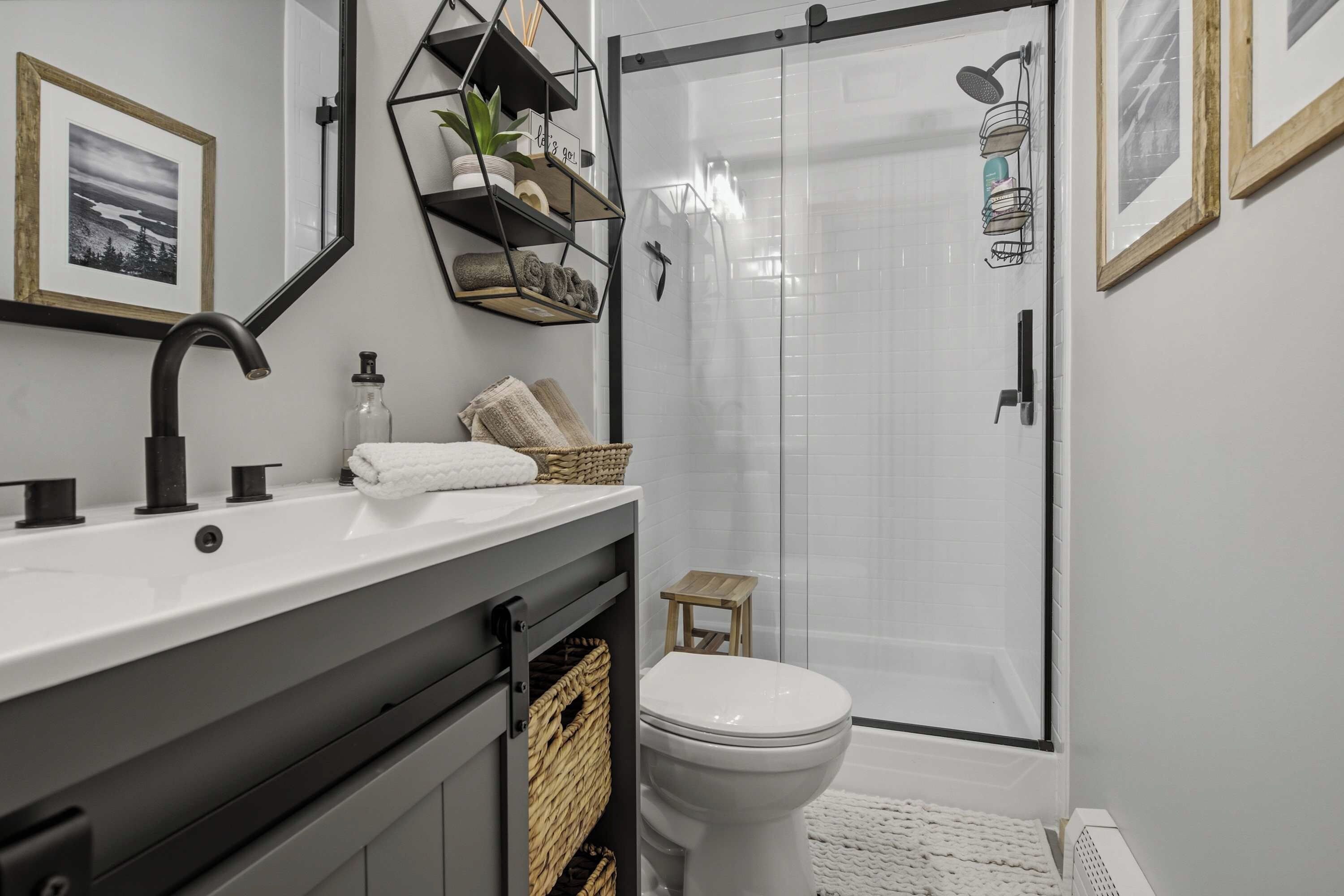 Un baño moderno con ducha, inodoro y lavamanos. Hay estantes con toallas y artículos de aseo.