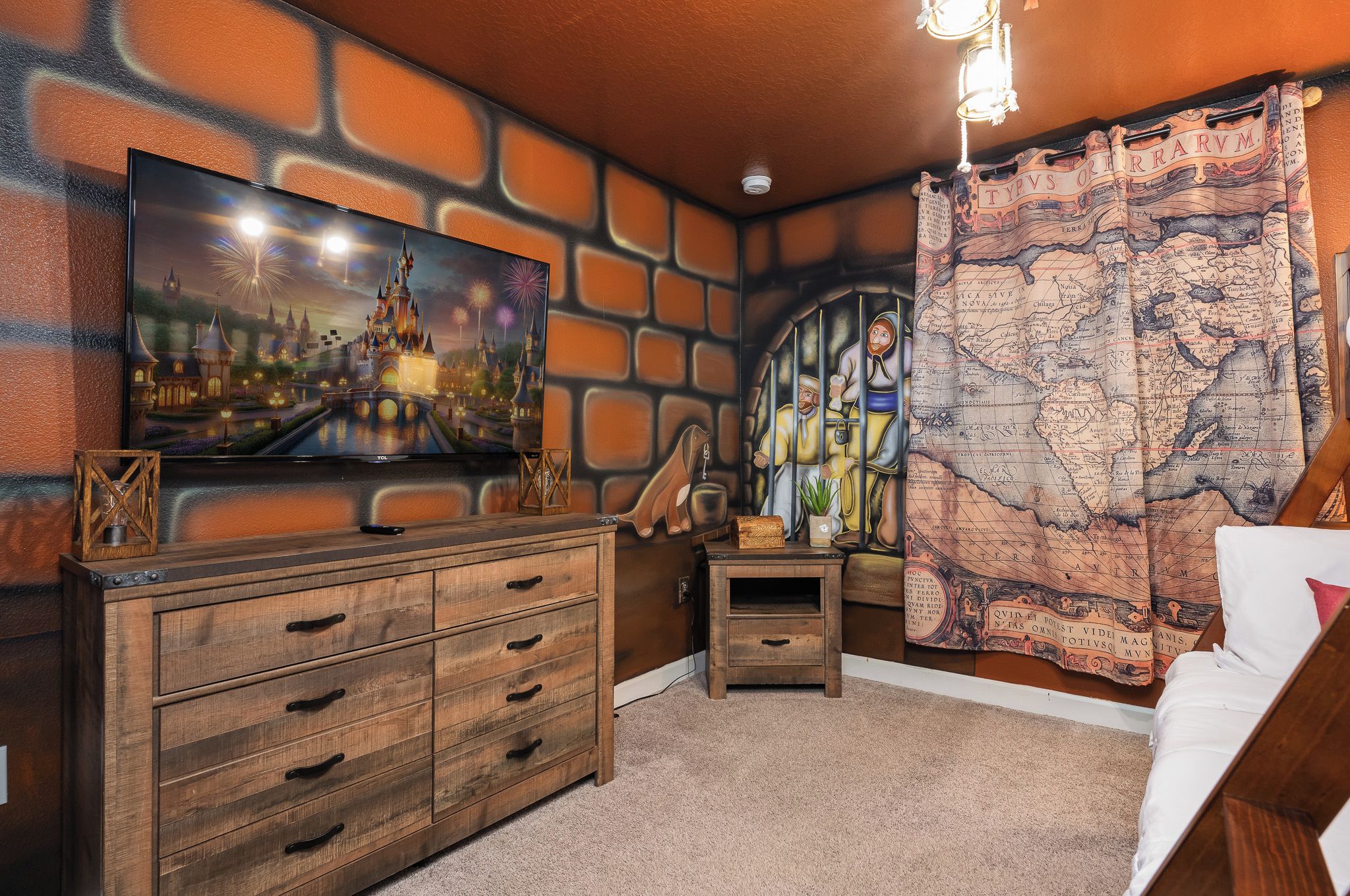 A room with a large flat-screen TV mounted on a brick-patterned wall, a wooden dresser with multiple drawers, a small table with a decorative item, and a map-themed curtain.