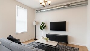 Ein modernes Wohnzimmer mit einer Couch, einem Couchtisch, einer Stehlampe, einem Fernseher und einer schwarzen Kommode.