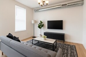 Een moderne woonkamer met een bank, een salontafel, een vloerlamp, een televisie en een zwarte kast.
