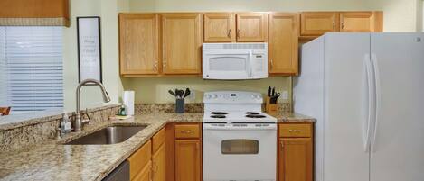 A kitchen with wooden cabinets, a white stove, a microwave, and a refrigerator.