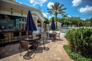 An outdoor bar area with wicker furniture and umbrellas, a pool, and palm trees. - 4BR corner townhome with 2 master suites (Davenport)