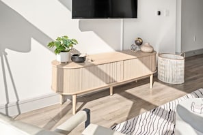 A modern living room with a wooden console table, a potted plant, a wall-mounted TV, and a woven basket. - Near NRG-Reliant, TMC, Downtown | Fast Wi-Fi (Houston)