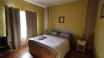 Une chambre à coucher comprenant un lit, une table de chevet, une chaise, une fenêtre avec des rideaux et un tableau accroché au mur.