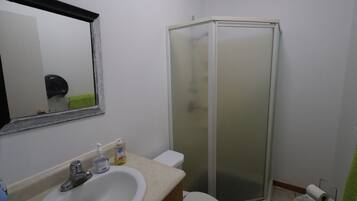 Een badkamer met een wit wastafelmeubel, toilet, douchecabine met glazen wanden en een spiegel met decoratieve lijst.