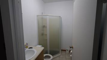 Un baño con inodoro, lavamanos y ducha con mampara de vidrio.